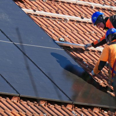 Zwei Handwerker installieren eine Solaranlage auf einem Hausdach.