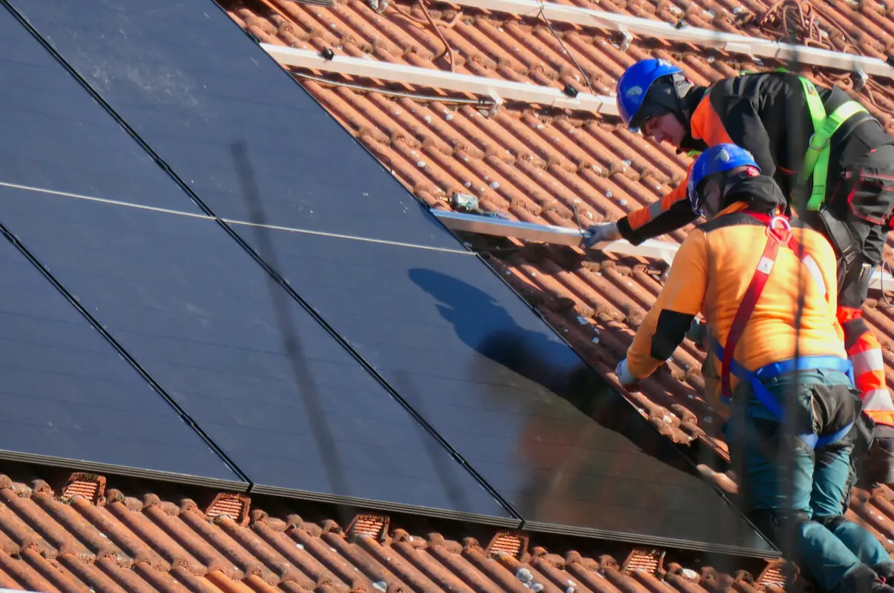Zwei Handwerker installieren eine Solaranlage auf einem Hausdach.