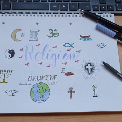 Auf einem Schreibblock wurden verschiedene religiöse Symbole gezeichnet; das Wort "Religion" steht im Mittelpunkt.