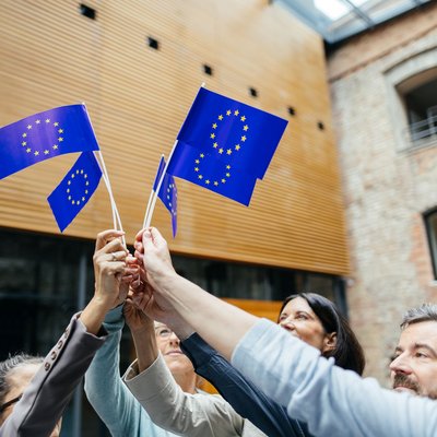 Auf dem Foto sieht man eine Gruppe von Menschen im Kreis, die jeweils eine EU-Fahne in die Mitte halten.