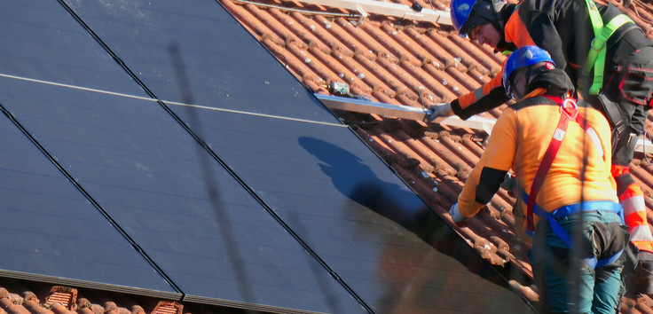 Zwei Handwerker installieren eine Solaranlage auf einem Hausdach.