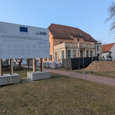 Auf dem Bild sieht man ein großes Baustellenschild, dass auf die Sanierung und dem Umbau des Amtshauses in Lehnin hinweist. AUßerdem auf die Fördergelder, die für dieses Projekt bereitgestelltu wurden. 