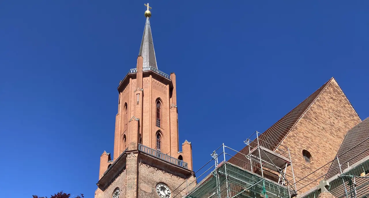 Man erkennt den Turm der St. Marien-Andreas Kirche in Rathenow vor blauem Himmel, ein Teil des davor abgebildeten Kirchenschiffs ist eingerüstet
