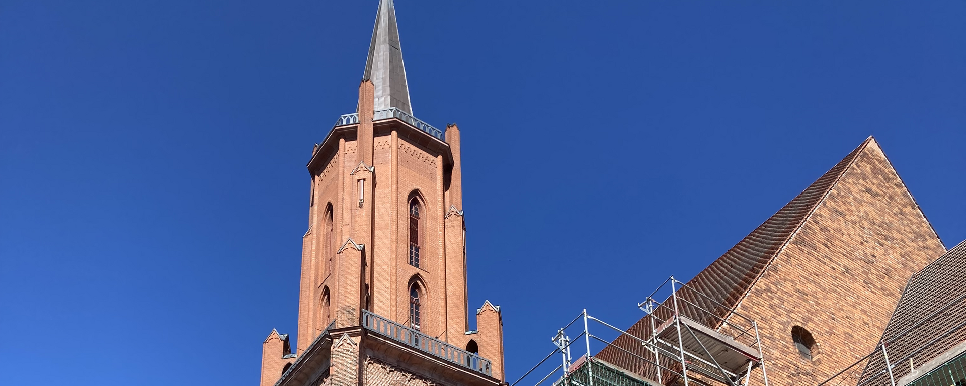 Man erkennt den Turm der St. Marien-Andreas Kirche in Rathenow vor blauem Himmel, ein Teil des davor abgebildeten Kirchenschiffs ist eingerüstet