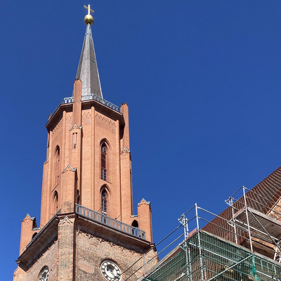 Man erkennt den Turm der St. Marien-Andreas Kirche in Rathenow vor blauem Himmel, ein Teil des davor abgebildeten Kirchenschiffs ist eingerüstet