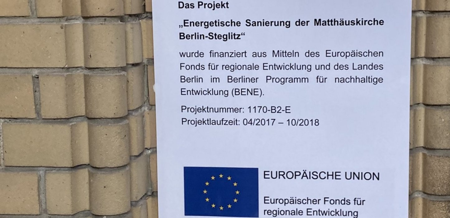Man erkennt einen Ausschnitt des EFRE-Förderschildes zum Projekt "Energetische Sanierung", Matthäuskirche Berlin-Steglitz auf einer Ziegelwand im Eingangsbereich.