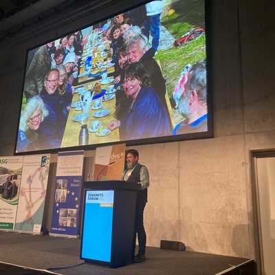 Man erkennt Pfarrer Schwieger von der NABU-Kirche Neu Temmen unter der Powerpoint-Präsentation mit einer Kaffetafel hinter dem Rednerpult im CityCube beim Zukunftsforum.